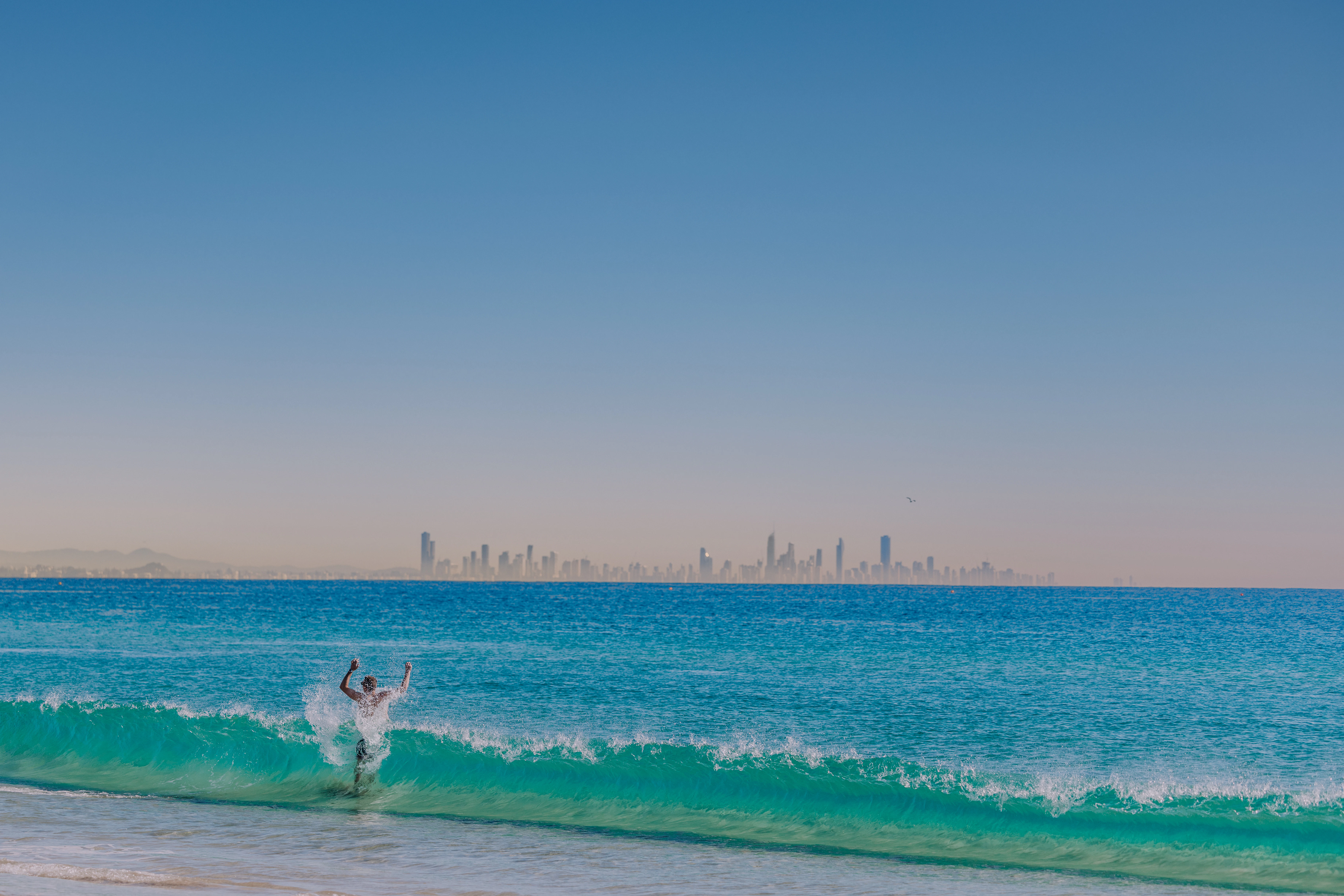 Surfer riding a wave with city skyline in distance