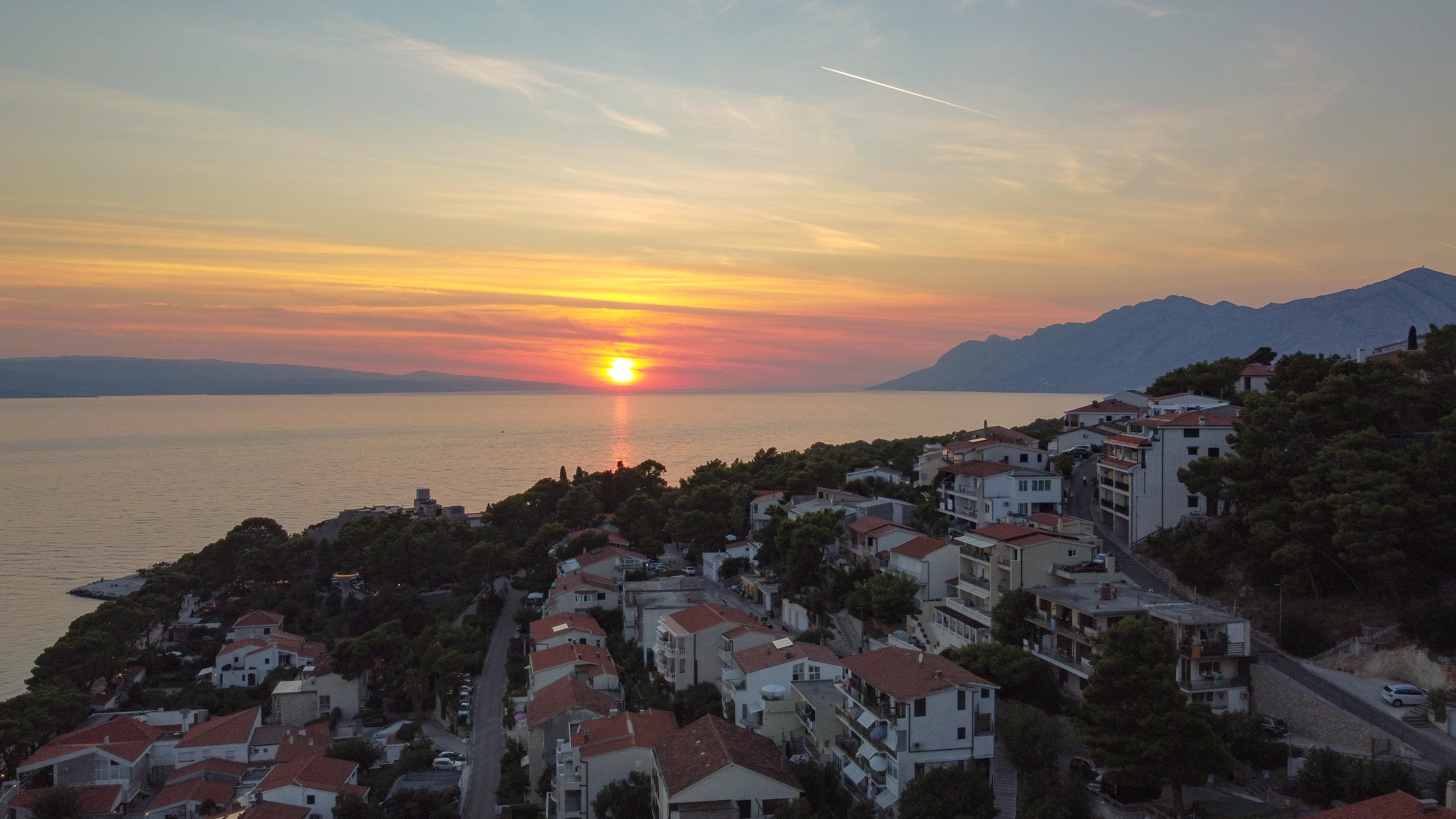 the sun is setting over a small town by the water