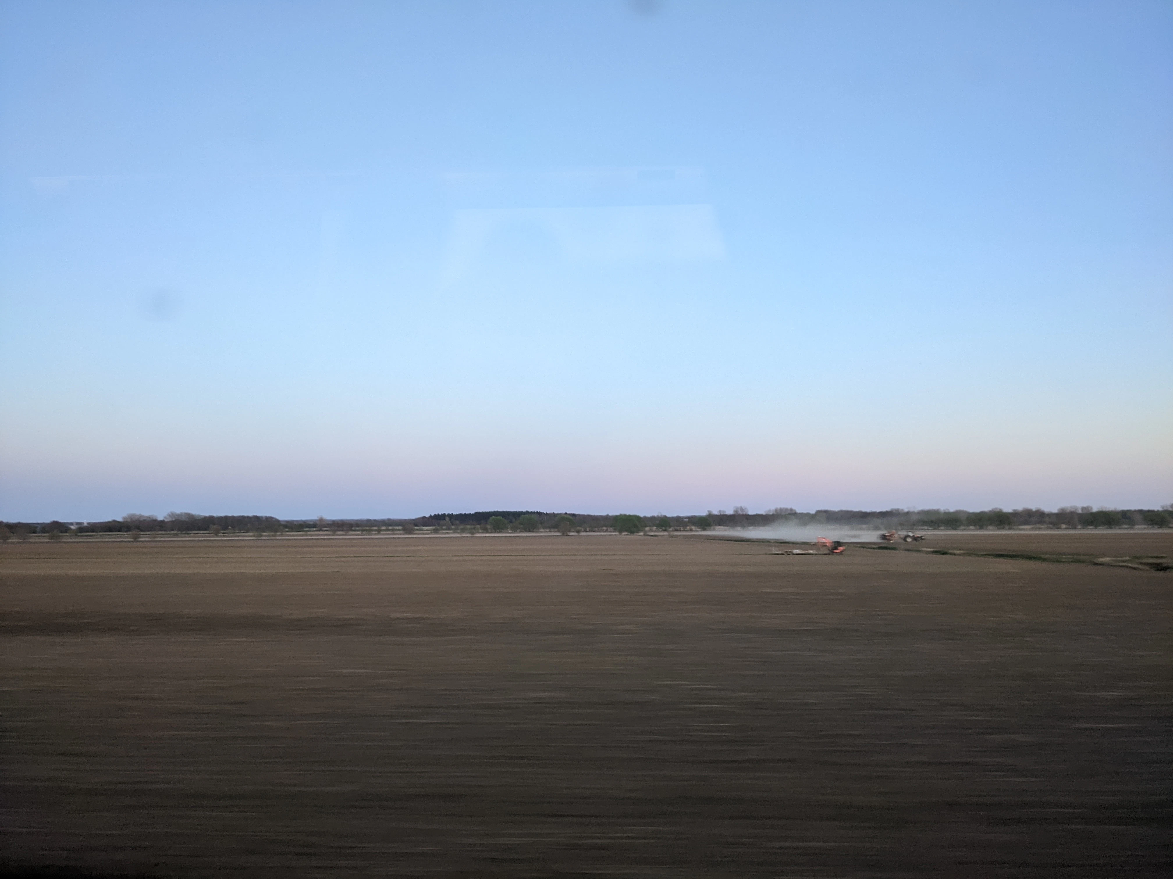 a large open field with a plane flying in the sky