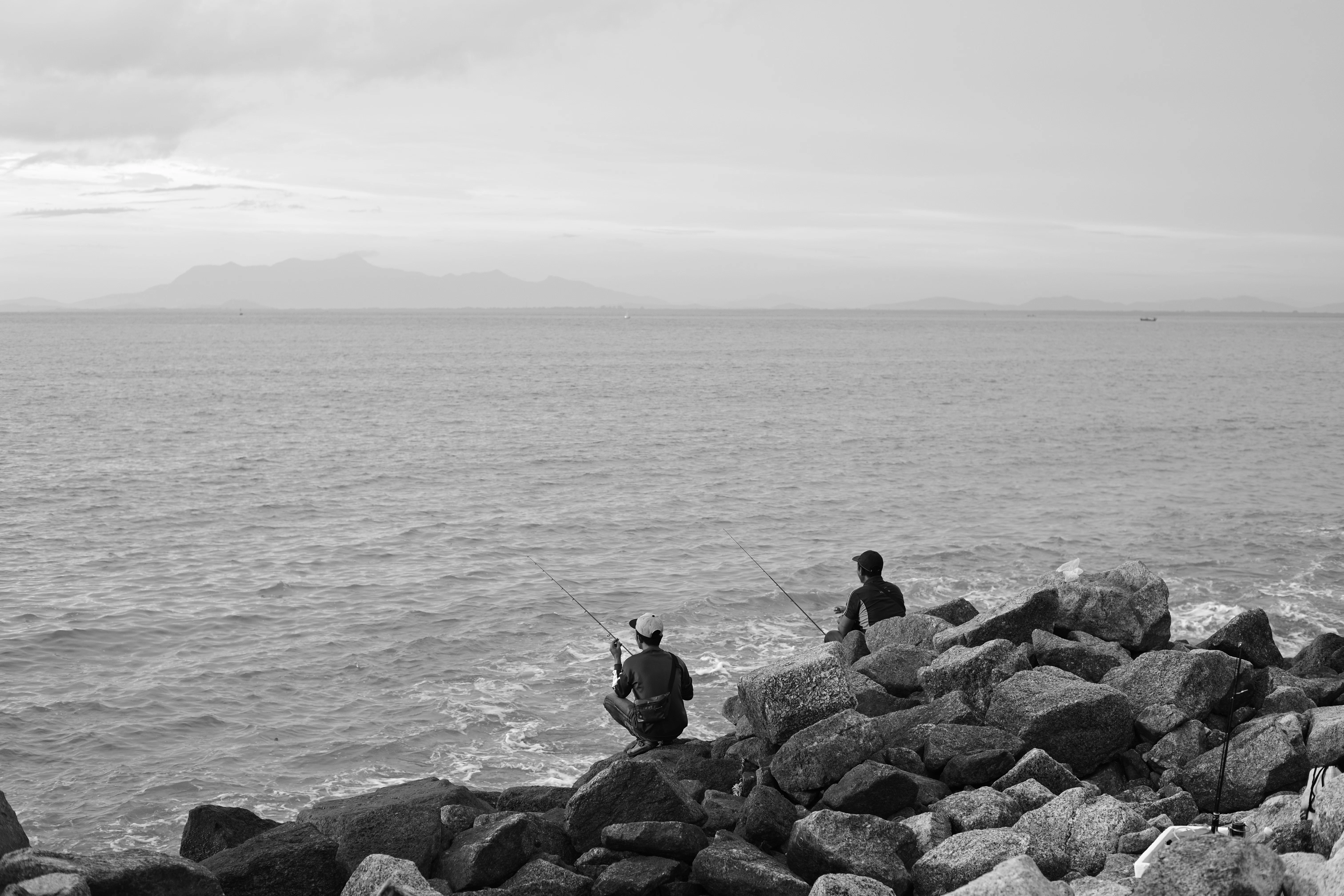 Two people are fishing by the ocean.