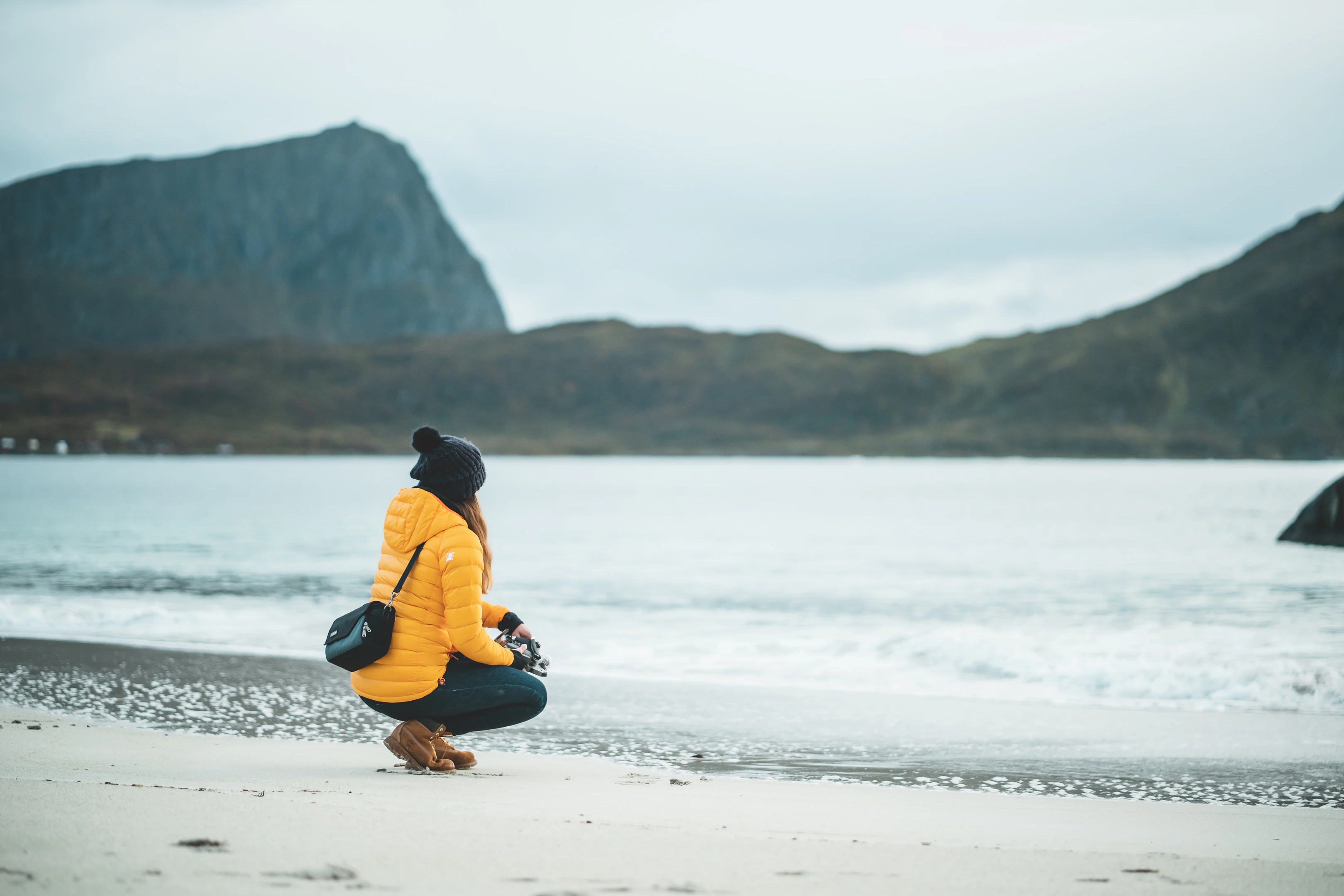 man in orange and blue jacket sitting on beach shore during daytime