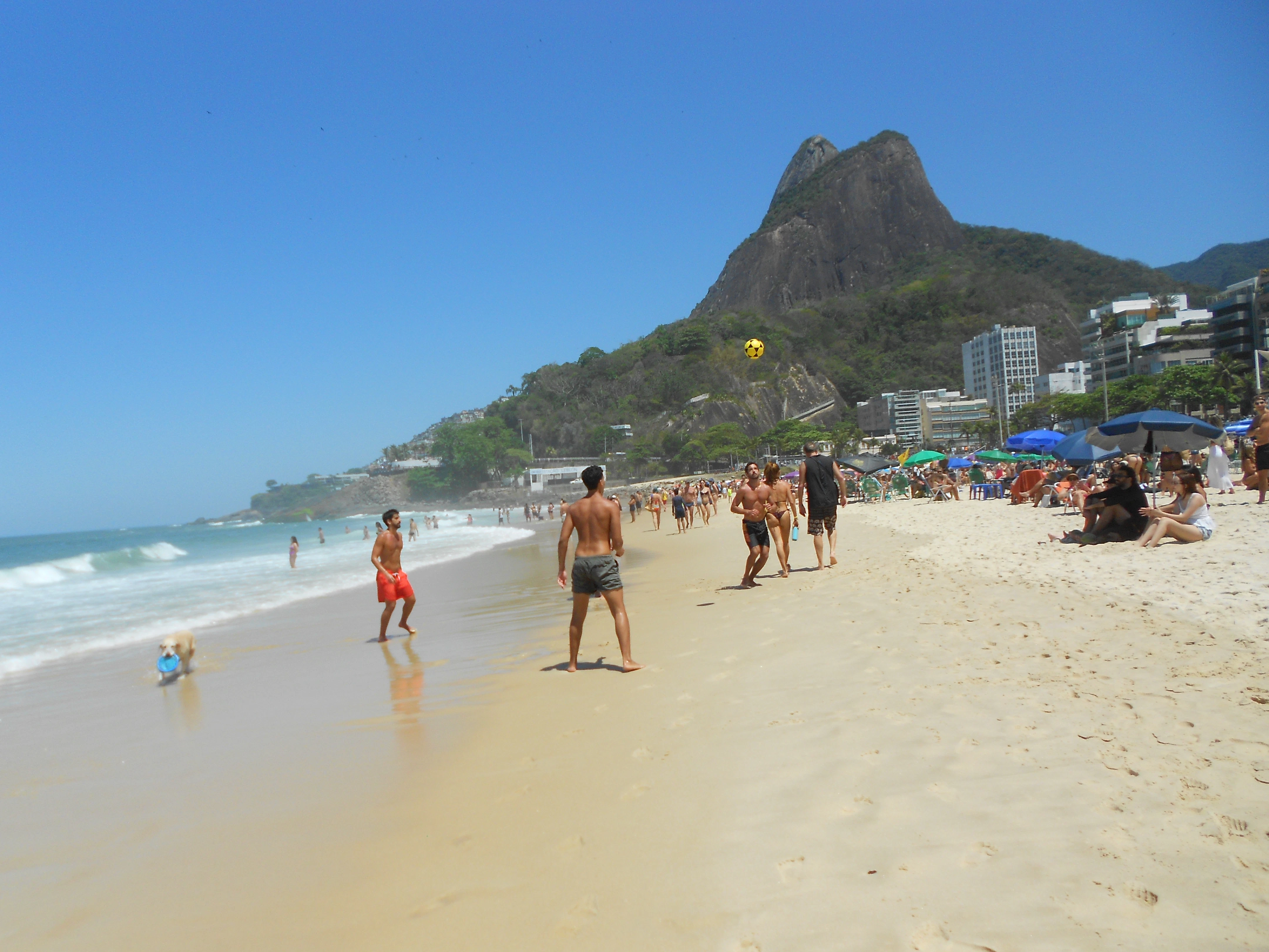 People playing volleyball on a sunny beach with mountain backdrop