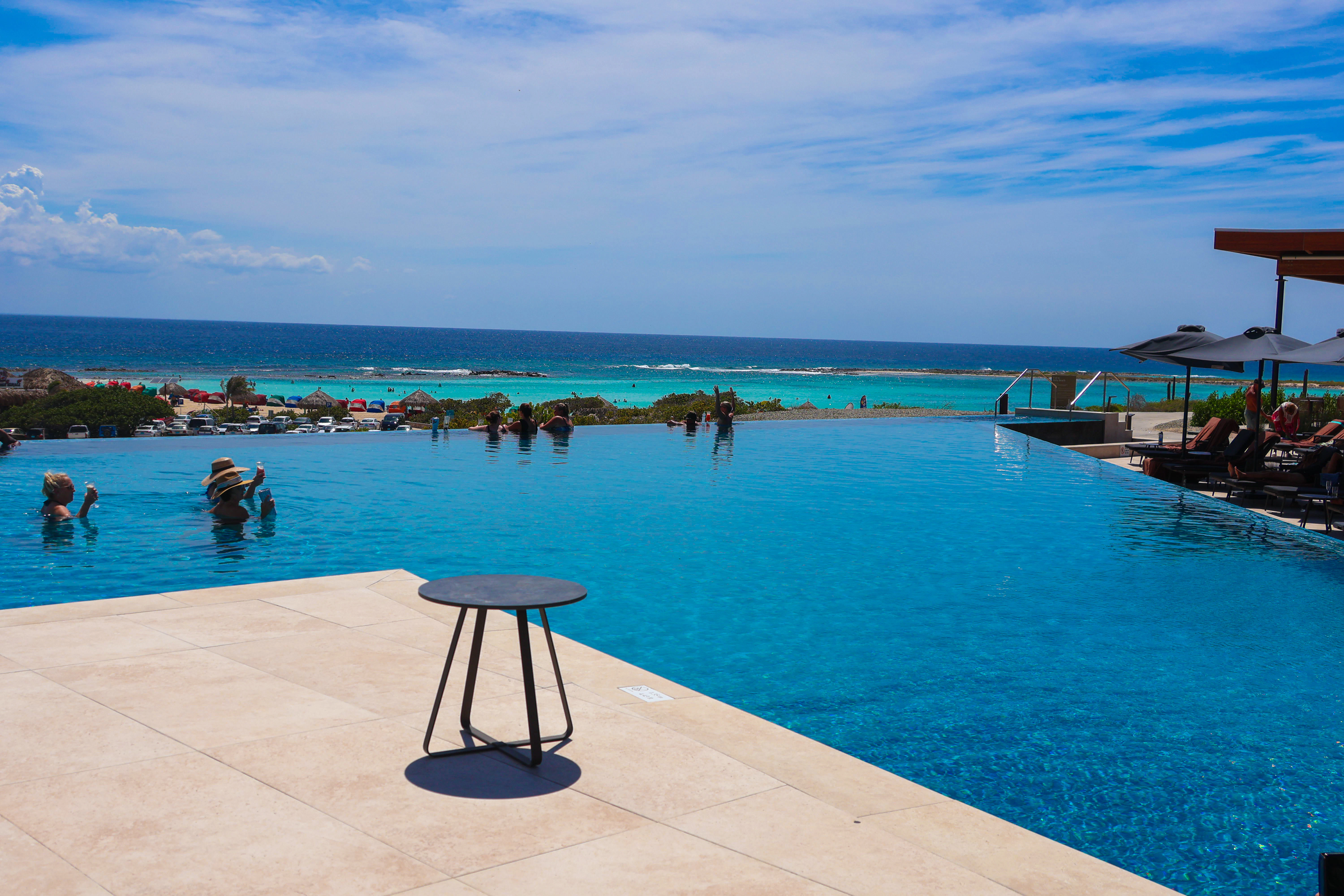 Infinity pool overlooking a turquoise ocean with people swimming.