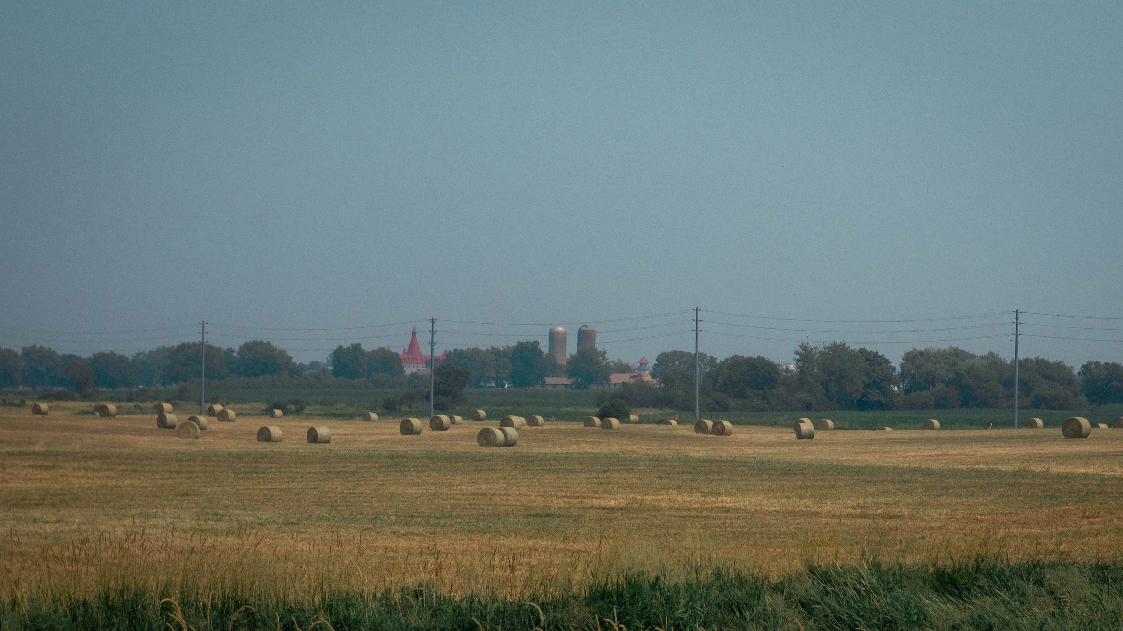 Hay bales sit in a field with a distant town.