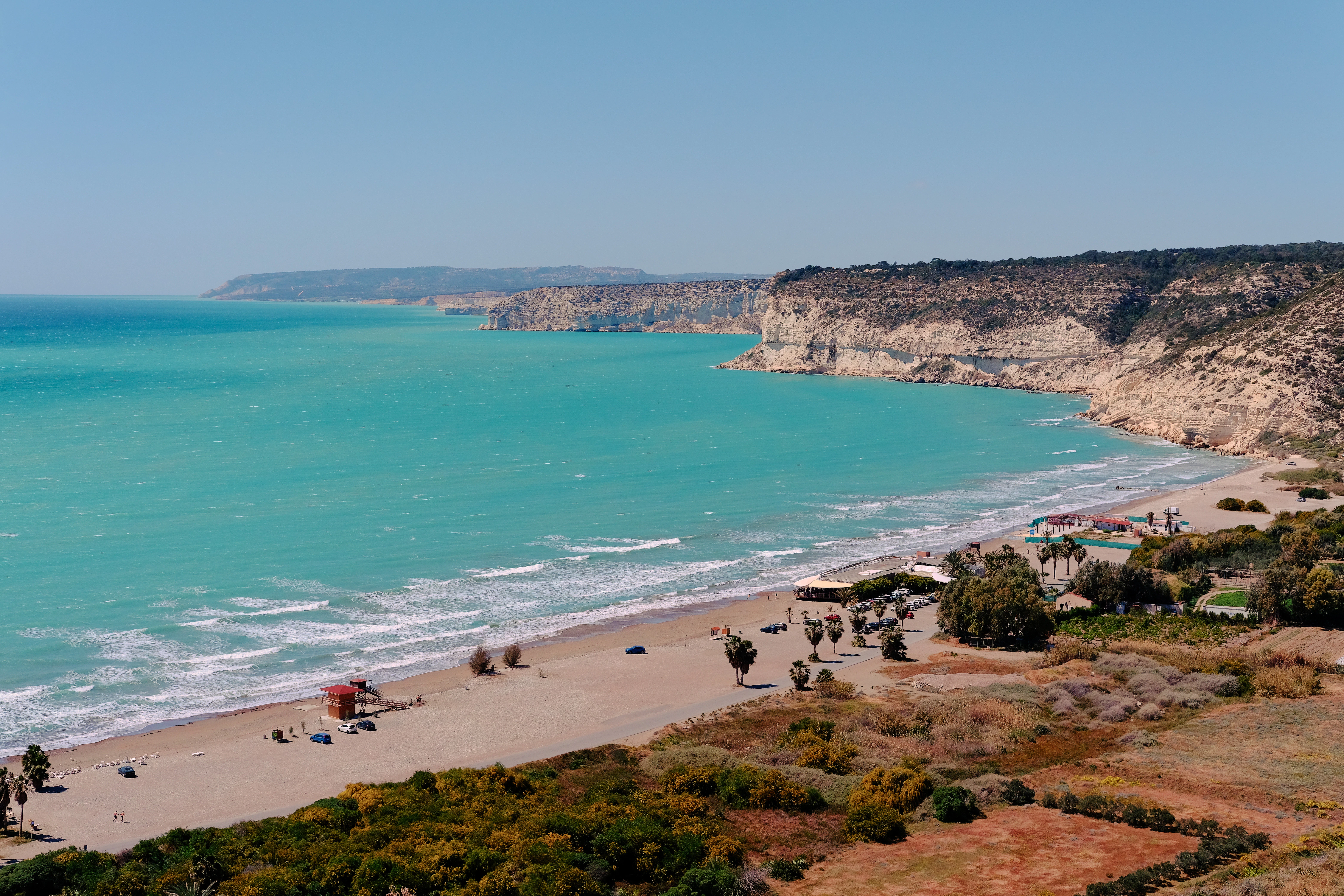Turquoise ocean meets sandy beach with cliffs.