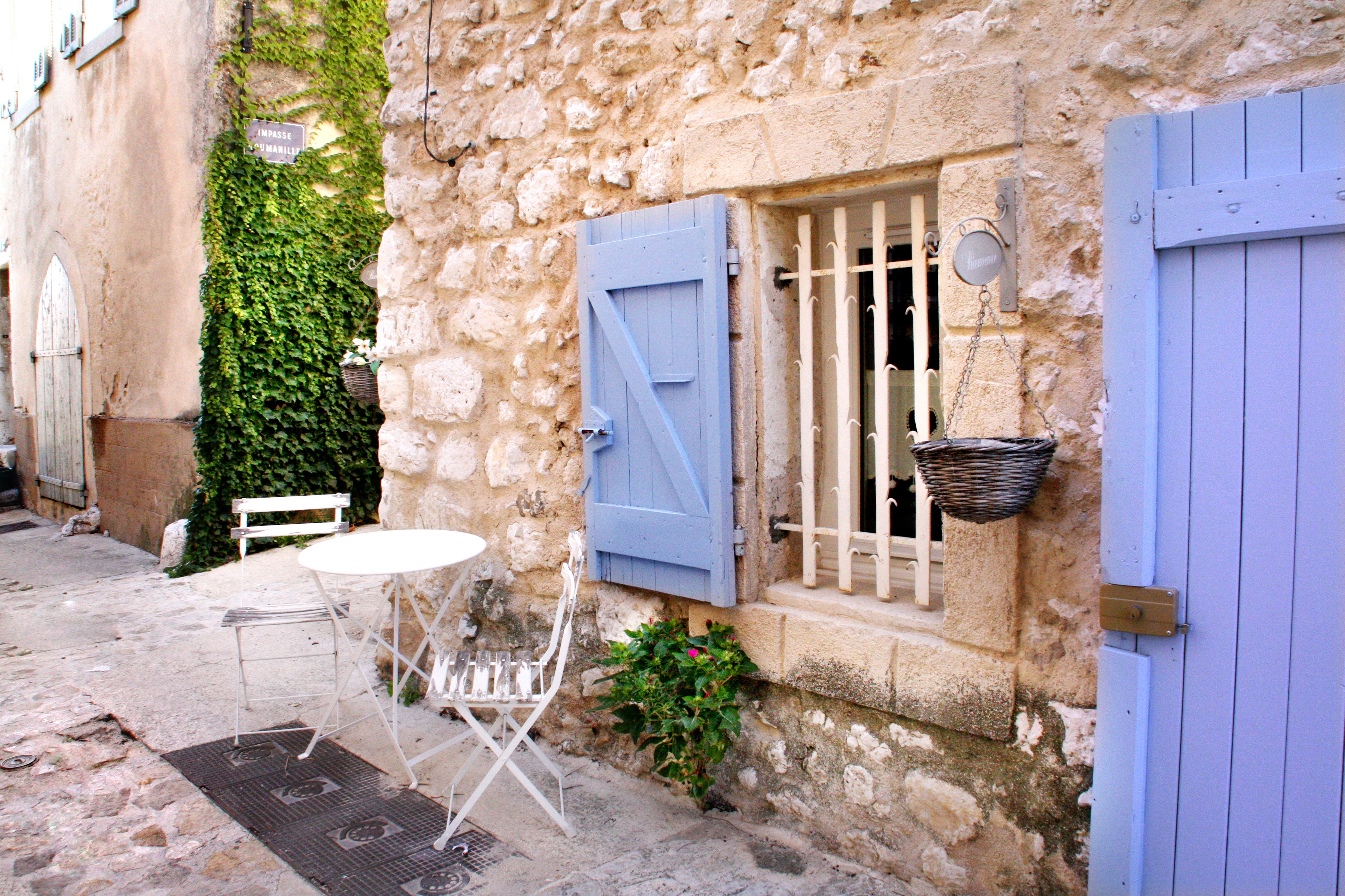 Charming stone building with blue shutters and outdoor seating.