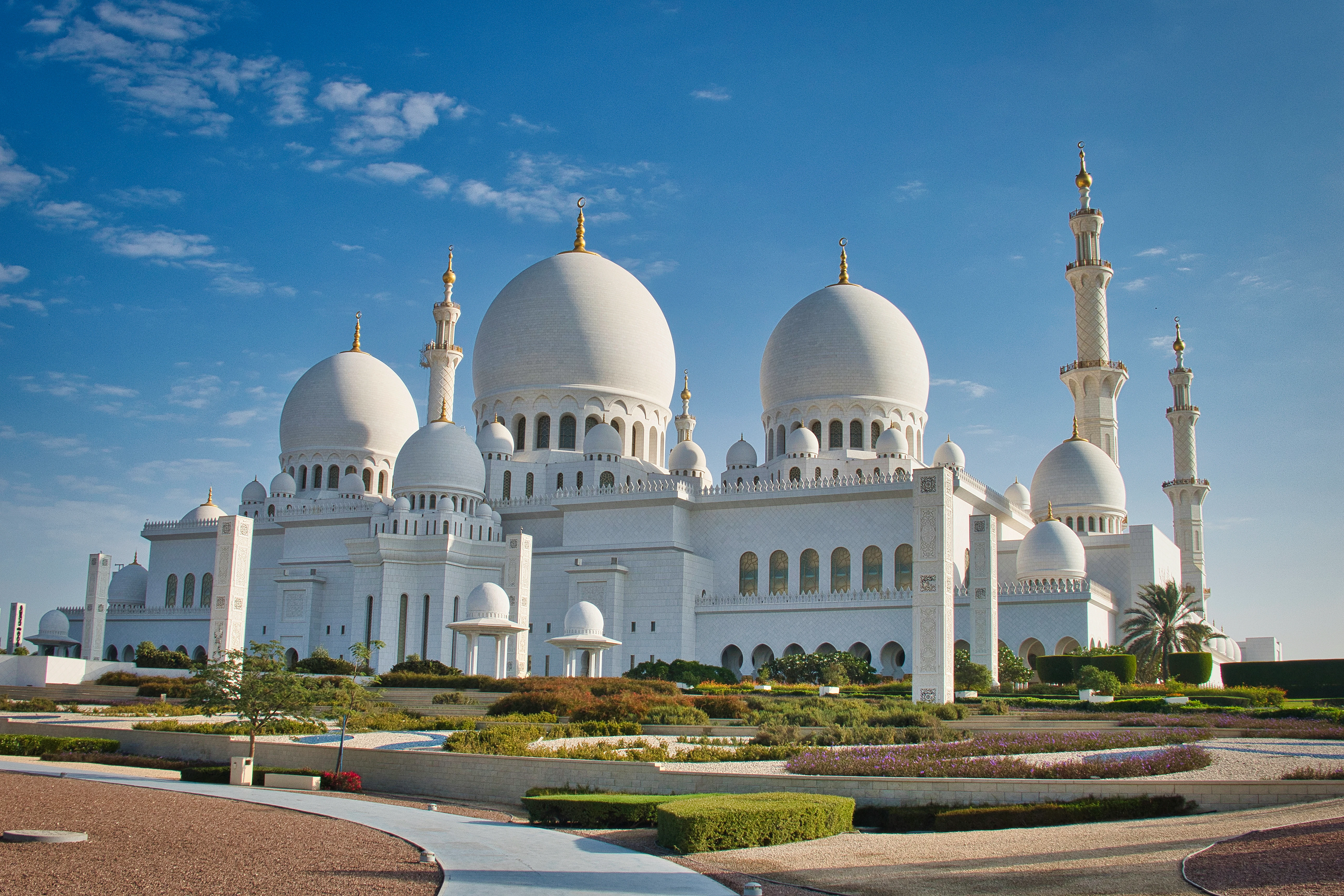 Grand white mosque with domes and minarets under blue sky.